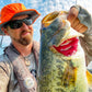 picture of a man holding a bass that he caught wearing a shelta sun hat and aquaterra sun shirt